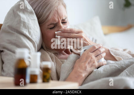 Kranke Frau mittleren Alters niesen Nase weht auf dem Bett sitzen Stockfoto