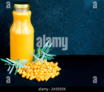 Flasche Sanddorn vitamin Saft und frischen Sanddornbeeren auf schwarzem Hintergrund. Kopieren Sie Platz. Stockfoto