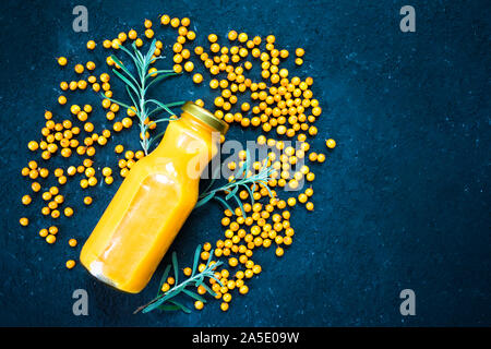 Flasche Sanddorn vitamin Saft und frischen Sanddornbeeren auf schwarzem Hintergrund. Ansicht von oben, kopieren. Stockfoto