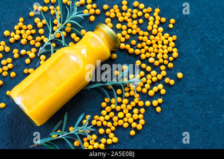 Eine Flasche Vitamin Saft aus Sanddorn und frischen Beeren Sanddorn auf schwarzem Hintergrund. Ansicht von oben. Stockfoto