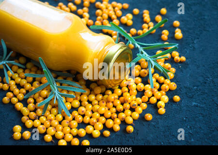 Eine Flasche Vitamin Saft aus Sanddorn und frischen Beeren Sanddorn auf schwarzem Hintergrund. Close-up. Stockfoto