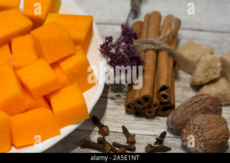 Gehackt Kürbis auf weiße Platte mit Zimtstangen, Anis*, Muskat und Nelken auf grau Holztisch Hintergrund. Zutaten zum Backen leckere Torte o Stockfoto