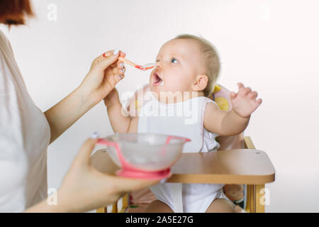 Mamma ihr Baby füttern mit dem Löffel. Mutter essen zu Ihrem 8-monatigen Kind zu Hause geben. Babynahrung Stockfoto