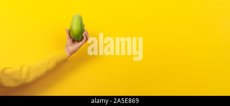 Frau Hand, grüne Papaya auf gelbem Hintergrund, gesunde Ernährung Konzept, Panoramic Image mit Platz für Text. Stockfoto