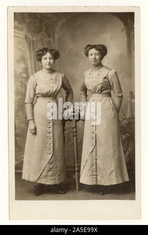 Original, klare Postkarte aus der frühen WW1. Jahrhundert mit attraktiven jungen Frauen, Schwestern wie Zwillingen - Geschwister in passenden Button-Down-Kleidern, Blusen, langem Saum, kleinen Taillen. Interessante Frisuren, Haare fegten auf der Seite. Datiert vom 6 1914. Juli auf der Rückseite, ein ergreifendes Foto, das Tage vor dem Ausbruch des ersten Weltkriegs in Großbritannien aufgenommen wurde Stockfoto