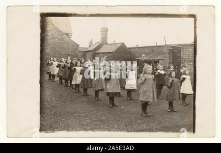 Originales charmantes Foto aus den frühen 1900er Jahren von viktorianischen Schülerinnen und Jungen, viktorianischen Schülerinnen, viktorianischen Schülerinnen, viktorianischen Schülern, viktorianischen Kindern, die elegante Kleidung tragen, Sport draußen, im Schulhof, Mädchen tragen Pinafores, Lehrer-Monitore, Überwachung, circa 1905, Großbritannien Stockfoto