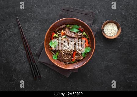 Pfannengerichte mit Soba Nudeln, Rind (Fleisch) und Gemüse. Asiatische gesundes Essen, gebratenes Essen in Schüsseln Rühren auf schwarzem Hintergrund, Ansicht von oben. Stockfoto