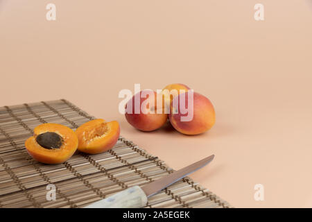 Aprikosen Früchte auf einem Pfirsich Farbe Hintergrund angeordnet, Obst schneiden und Messer auf einem Holztisch mat Stockfoto
