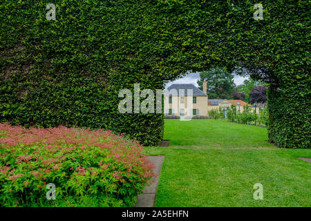 Blick auf ein traditionelles Gebäude durch die Öffnung in der langen Buchse Zaun an der Royal Botanic Garden in Edinburgh, Schottland Stockfoto