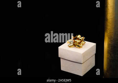 Isolierte einzelne Geschenkbox mit goldener Dekoration auf schwarz und gold Hintergrund. Stockfoto