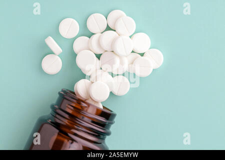 Weiße, runde Tabletten vor Glas Flasche Pillen verstreut Stockfoto