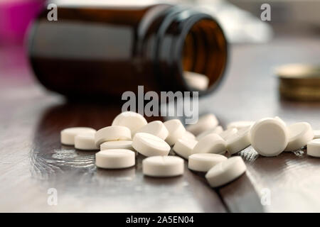 Weiße, runde Tabletten vor Glas Flasche Pillen verstreut Stockfoto