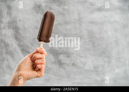 Frau mit Eskimo Pie Eis in der Hand auf grauem Hintergrund. Eskimo Pie tag Konzept Stockfoto