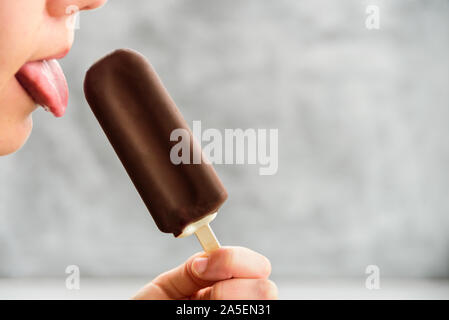 Frau lecken Zunge Eskimo Pie Eis auf grauem Hintergrund. Eskimo Pie tag Konzept Stockfoto