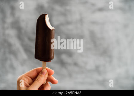 Woman Holding aus Eskimo Pie Eis in der Hand auf grauem Hintergrund gebissen. Eskimo Pie tag Konzept Stockfoto