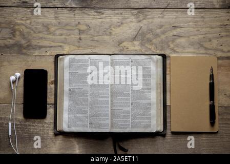 Overhead Aufnahme der geöffneten bibel in der Mitte eines Notebook und Smartphone auf einer Holzoberfläche Stockfoto