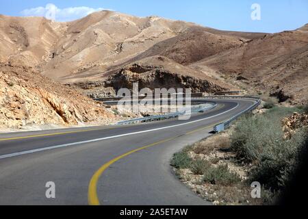 Curvy sandigen Weg auf einer Landstraße, die sich entlang des Toten Meeres läuft von einer Seite und Edom Berge bei Arava Wüste vom Anderen in Israel. Stockfoto