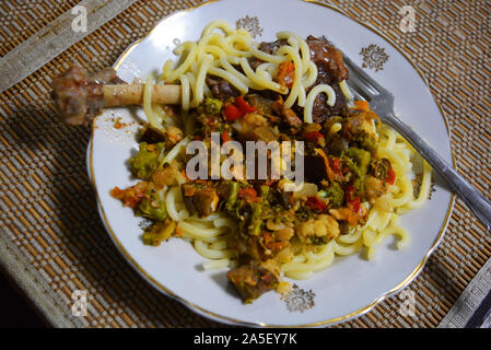 Geschmorte Bein einer hausgans mit überprüften Ukrainischen Nudeln und gewürzt mit Gemüse von Auberginen, Möhren, Zwiebeln und Brokkoli. Stockfoto