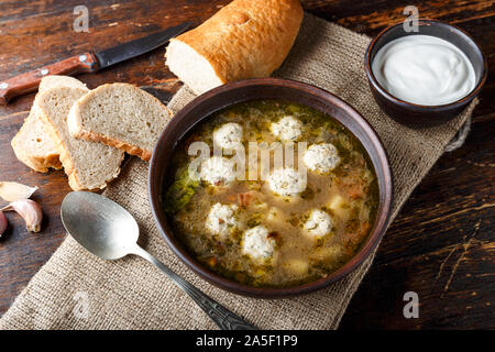 Hausgemachte Suppe mit Fleischbällchen in einem Ton Teller auf dem Tisch. Platte steht auf einem sackleinen Serviette. Hot home Abendessen Stockfoto