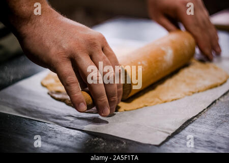 Bäcker Händen rollen Ingwer Teig auf einem dunklen Hintergrund. Nahaufnahme, Soft Focus. Seitenansicht, Draufsicht. Kopieren Sie Platz. Stockfoto