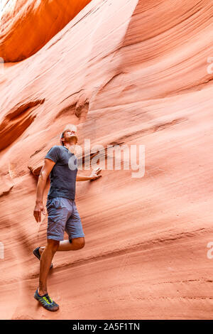 Mann Wanderer Klettern Suchen berühren Wand der roten Welle Form Formationen vertikale Ansicht auf Antelope Slot Canyon in Arizona am Wanderweg Wanderweg vom See Stockfoto