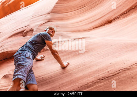 Mann Wanderer Klettern bis zu berühren Wand der roten Welle Form formationen Blick auf Antelope Slot Canyon in Arizona am Wanderweg Wanderweg von Lake Powell. Stockfoto