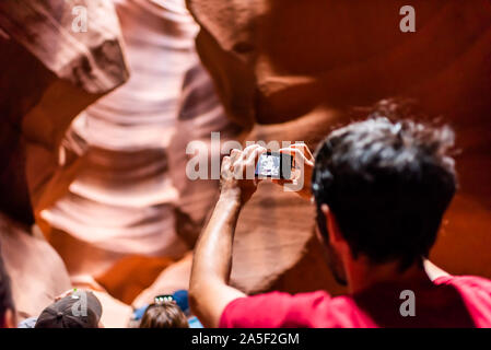 Seite, USA - 10. August 2019: Tour Gruppe junger Mann zurück in Upper Antelope Slot Canyon in Arizona Aufnehmen von Bildern mit der Kamera aus Sandstein Format Stockfoto