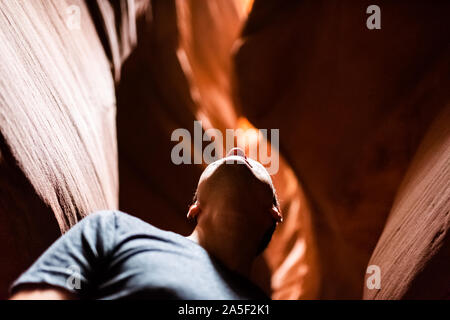 Low Angle View des jungen Mannes in Upper Antelope Slot Canyon in Arizona, Dark Rock Sandstein Wellenform Formationen auf der Suche Stockfoto