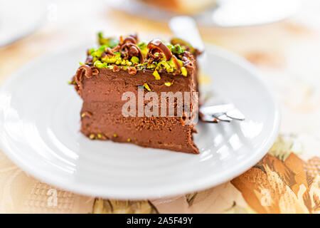 Closeup makro Blick auf hausgemachte layered Pistazie Schokolade raw vegan Kuchen Slice auf weiße Platte mit Schokolade Spänen und Mutter grün Stück Textur Stockfoto