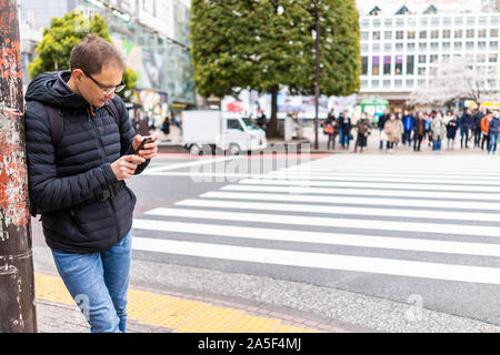 Tokio, Japan berühmten Shibuya Crossing crosswalk in Downtown City mit man touristische stehend an Richtungen auf Telefon Stockfoto