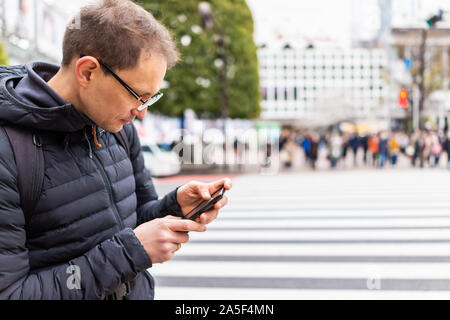 Tokio, Japan berühmten Shibuya Crossing in der Innenstadt von Stadt mit man touristische stehend an Richtungen auf dem Telefon suchen von Zebrastreifen Stockfoto