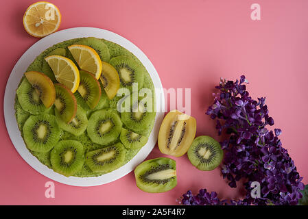 Kalten Kuchen mit Kiwi und Cashew Nüssen garniert mit Scheiben von Kiwi, Himbeeren und Brombeeren auf einem rosa Hintergrund Stockfoto