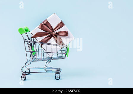 Geschenkbox mit braunen Bug in Miniatur Einkaufswagen in Pastell-blaue Hintergrund mit kopieren. Stockfoto