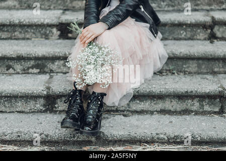 Frau in rosa spitze Rock mit weißen Blumen in den Händen Blumenstrauß sitzt auf der Treppe. Stockfoto