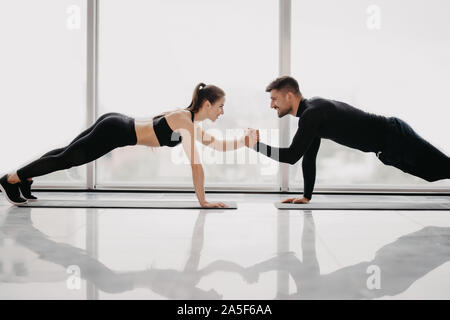 Junges sportliches Paar aus gemeinsam in ein Fitnessstudio. Dabei plank Übungen, während jeder andere Holding für eine Hand. Stockfoto