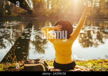 Reisende entspannen im Herbst River bei Sonnenuntergang. Junge Frau Touristen sitzen auf der Bank und halten die Hände hat. Herbst Aktivitäten Stockfoto