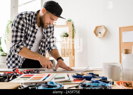 Die jungen kreativen Menschen in casualwear Biegen über Arbeitsplatz beim Vorbereiten der Werkstücke für dekorative pet Halsbänder im Studio Stockfoto