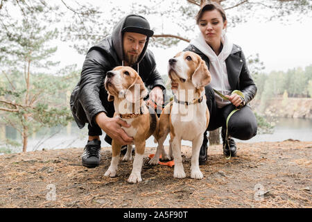 Junge casual Paar sitzt auf hockt kuscheln Zwei reinrassige Beagle Welpen beim Chillen in ländlicher Umgebung Stockfoto