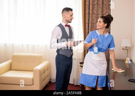 Hübsche Zimmermädchen in Uniform Reinigung Tabelle bei Porter mit Tablet suchen während des Gesprächs bei der Arbeit im Hotel Stockfoto