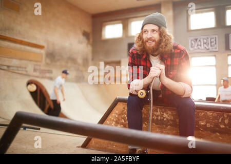 Porträt des zeitgenössischen bärtiger Mann weg schauen und lächeln, während die Standortwahl auf der Rampe in Skating Park, Kopie Raum Stockfoto