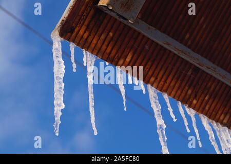 Viele der großen und scharfen Eiszapfen hängen auf dem Dach des Hauses. Jahreszeiten. Stockfoto