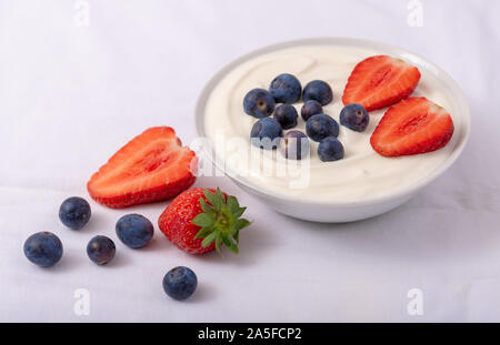 Joghurt in Weiß Schüssel mit Erdbeeren und Blaubeeren auf weißem Hintergrund. Stockfoto