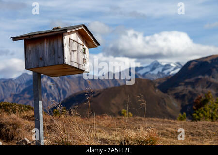 Eine kleine handgefertigten Holzmöbeln Vogel Haus auf einem Pfosten stehend auf einem Berg in den Alpen. Im Hintergrund die Gipfel im Schnee sind viisible. Stockfoto