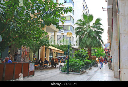 Athen, Attika, Griechenland - 17. Oktober 2018: Touristen wandern und Shopping entlang einer von Bäumen gesäumten Straße in Athen, Griechenland in der Nähe von einem Cafe. Stockfoto