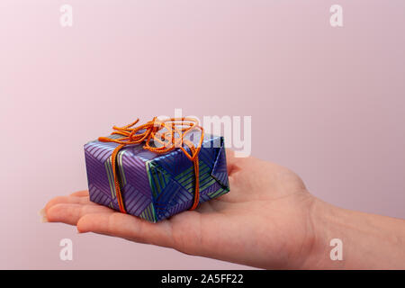 Ein blauer Geschenkkarton liegt auf einem offenen Frau Palm. Das Geschenk wird mit einem orangefarbenen Seil gebunden. Rosa Hintergrund. Stockfoto