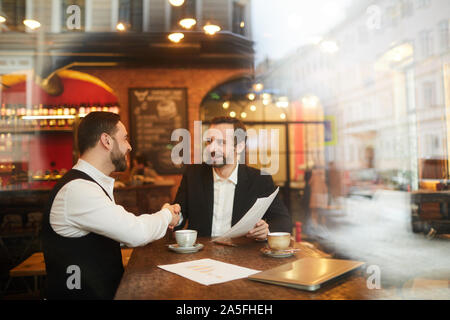 Durch das Glas Porträt von zwei erfolgreiche Geschäft Leute die Hände schütteln nach Vertragsabschluss während der Sitzung im luxuriösen Restaurant, Kopie Raum Stockfoto