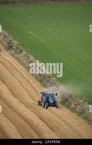 Ein Landwirt Pressen von Stroh in einer teilweise Abgeernteten Feld Neben einem trockenen Steinmauer in Aberdeenshire Stockfoto