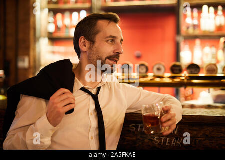 Seitenansicht Portrait von bärtigen reife Geschäftsmann Whiskey trinken und entspannen Sie in der Bar nach der Arbeit Stockfoto