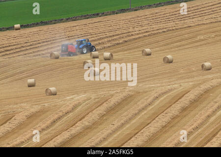 Ein Landwirt Pressen von Stroh in einer abfallenden Feld mit Strohballen Warten auf Sammlung Stockfoto