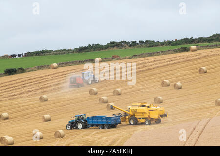 Ein Mähdrescher Off-Loading Korn in einen Anhänger und ein zweiter Traktor Pressen im gleichen Feld in Aberdeenshire Stockfoto